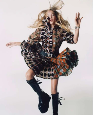 Model jumping in the air wearing a patterned printed dress and black platform boots against a white background.