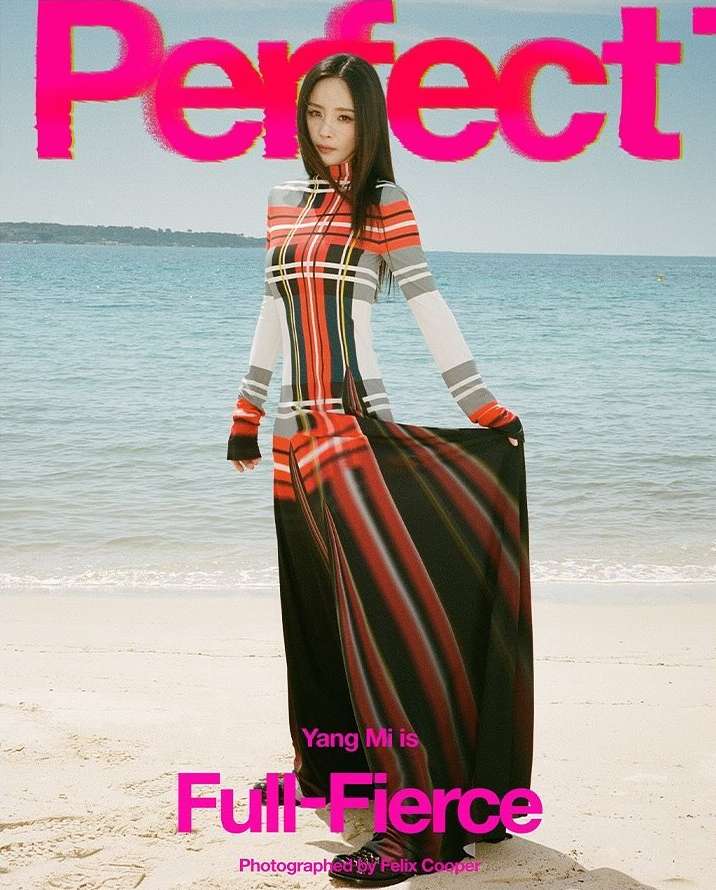 Asian woman in long plaid dress on a beach, magazine cover, bright pink masthead and text overlay, blue sky, sandy beach.