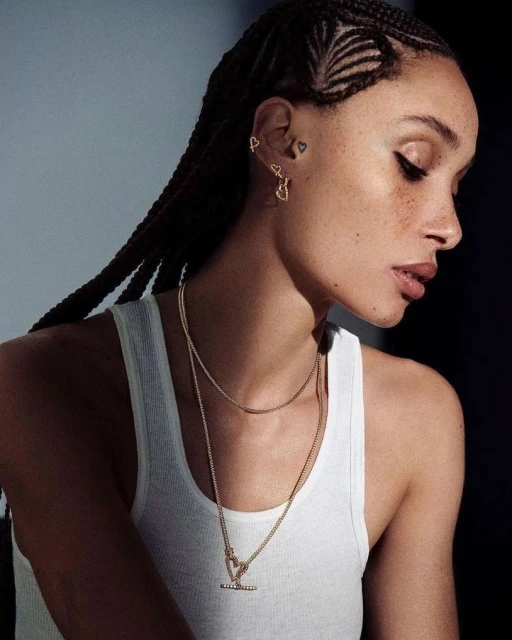Close-up of a woman with braided hair wearing a white tank top and gold heart jewelry, showcasing beauty and fashion details.