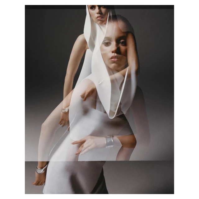 Portrait of two fair-skinned adult females posing in layered white hooded dresses against a gray backdrop with studio lighting.