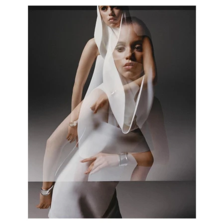 Portrait of two fair-skinned adult females posing in layered white hooded dresses against a gray backdrop with studio lighting.