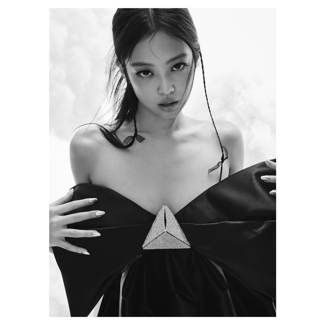 Monochrome portrait of a stylish woman with dark hair wearing a striking black dress with a large decorative triangle, in a photo studio.