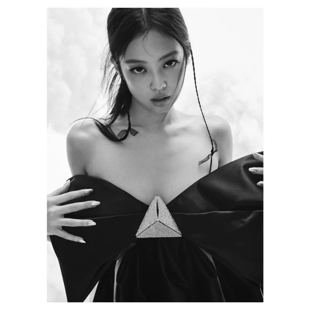 Monochrome portrait of a stylish woman with dark hair wearing a striking black dress with a large decorative triangle, in a photo studio.