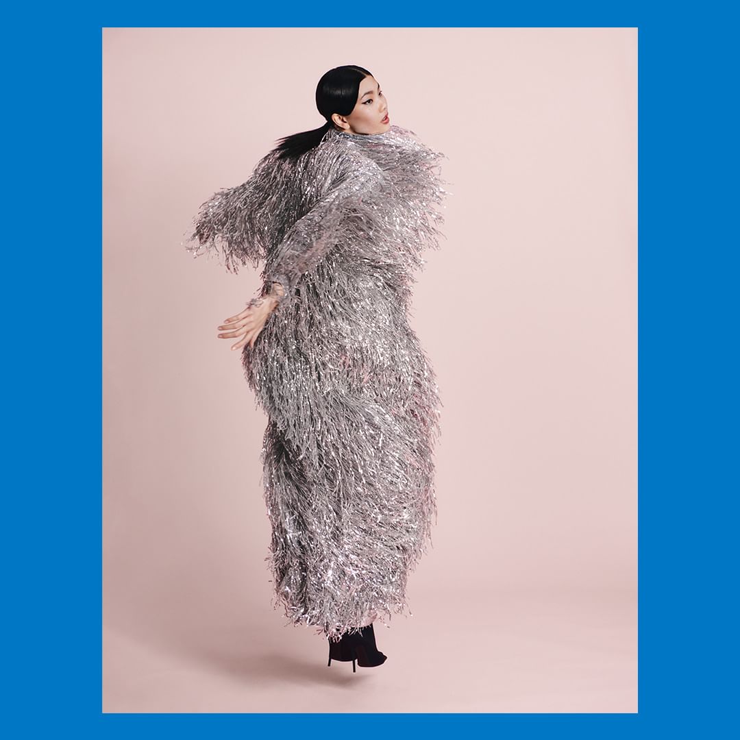Woman in a shiny silver fringed coat jumps in a pink studio. High fashion, studio shot, light pink backdrop, full body, fashion concept.