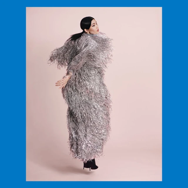 Woman in a shiny silver fringed coat jumps in a pink studio. High fashion, studio shot, light pink backdrop, full body, fashion concept.