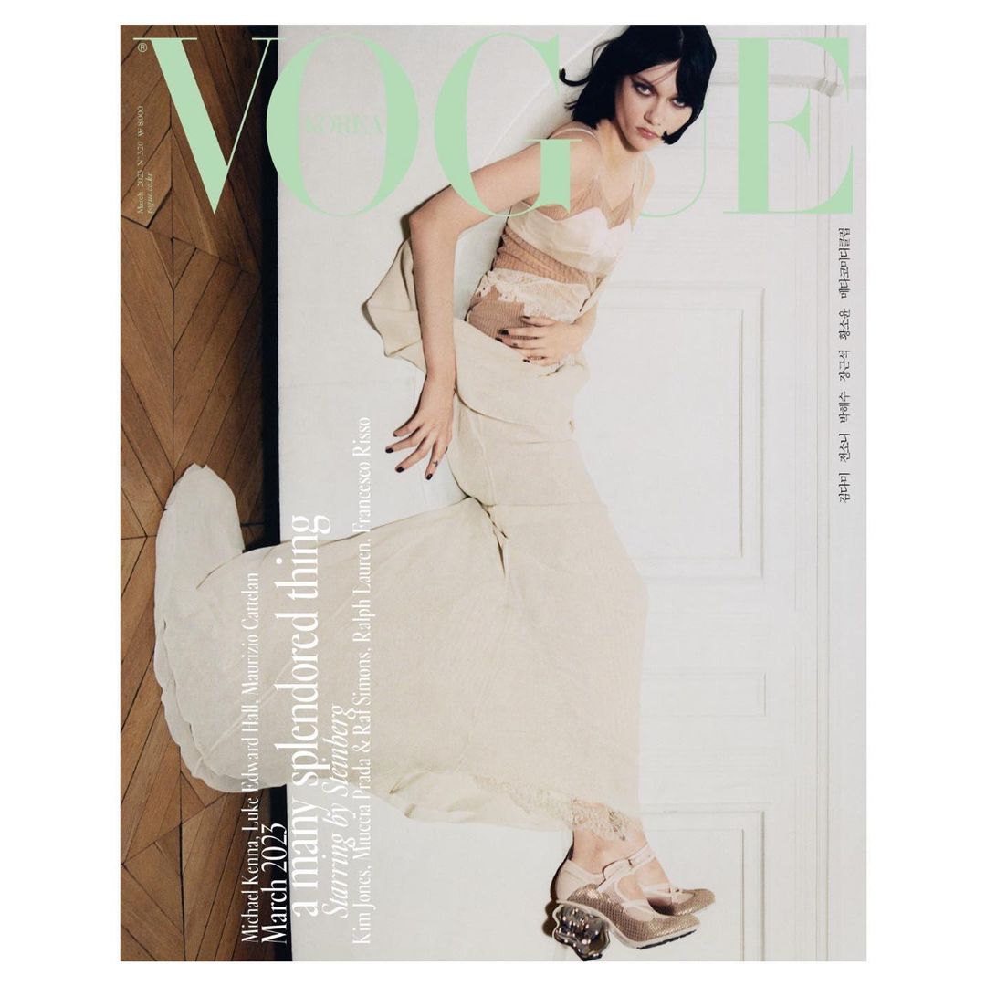 Vogue cover featuring a young woman with dark hair wearing a light-colored dress and shoes, posing against a neutral backdrop. Fashion editorial.