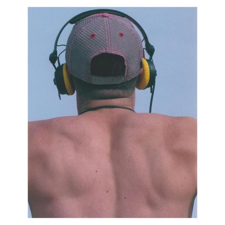Back view of shirtless adult wearing a baseball cap and black headphones with yellow earpads against light blue sky backdrop.
