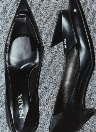 A pair of sleek black Prada heels is captured from a high angle against a textured gray background, highlighting their elegant design.