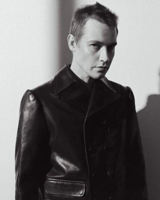 Black and white portrait of an adult male wearing a dark, double-breasted leather coat, looking at the camera with a neutral expression.