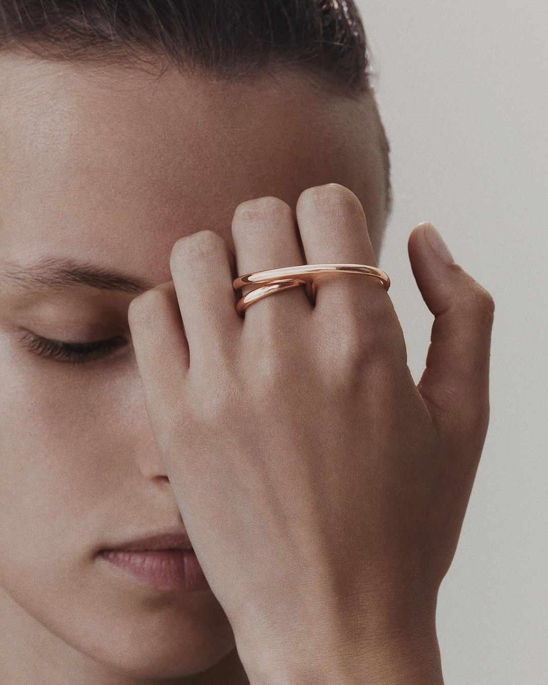 Close-up of a hand adorned with a distinctive rose gold ring, featuring a unique horizontal design, against a neutral backdrop.