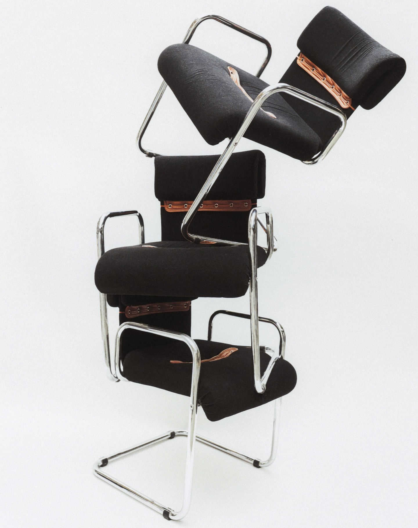 Three black cantilever chairs are stacked in a tower-like formation against a white background, showcasing minimalist furniture design.