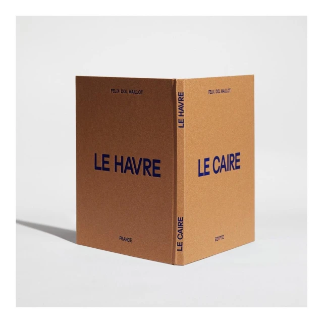 Two tan-colored hardcover books standing side by side, each featuring navy blue lettering: 'Le Havre' and 'Le Caire' against a bright backdrop.