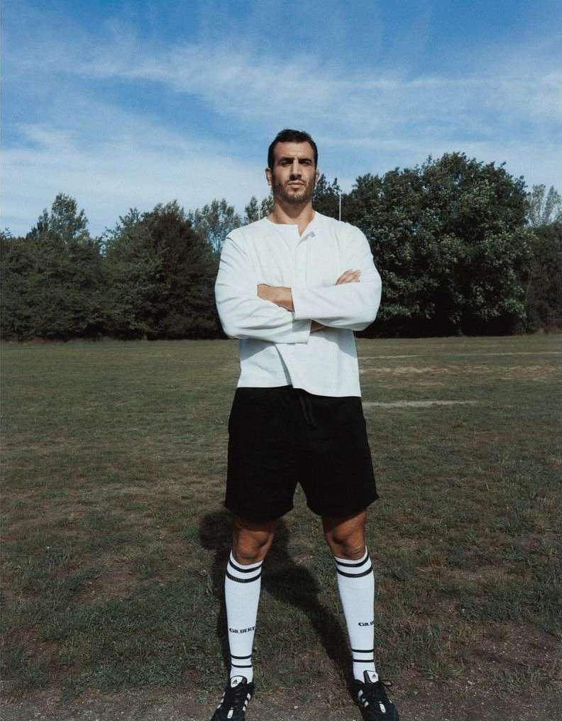Portrait of a soccer player standing on a grassy field with arms crossed. He is wearing a soccer uniform with long white socks.