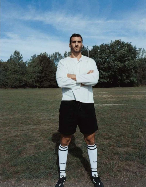 Portrait of a soccer player standing on a grassy field with arms crossed. He is wearing a soccer uniform with long white socks.