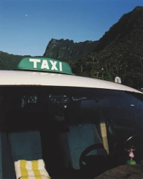 Close-up of a white taxi roof with a green sign and mountains in the background under a blue sky.