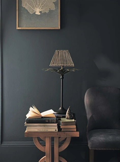 Interior decor showcasing a palm lamp, books on a wooden table, and a framed art piece against a dark blue wall, creating a cozy ambiance.