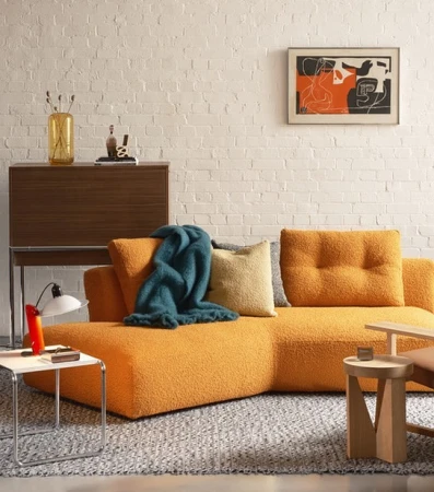 Living room interior featuring a cozy orange sofa with a teal throw blanket, complemented by modern furniture and decor against a white brick wall.