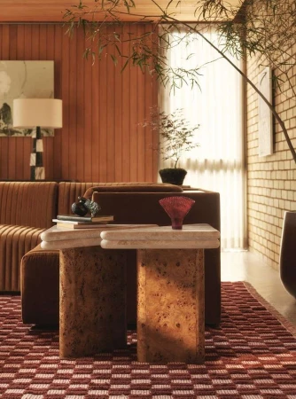 Living room interior featuring a brown corduroy couch, stone side tables, a red patterned rug, and decor accents like plants and lamps.