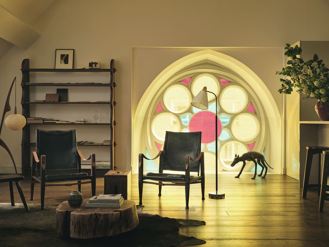 Living room interior with two black armchairs, a round wooden coffee table, and a dog sculpture in front of a decorative window.