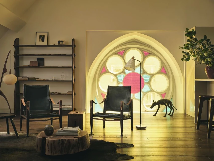 Living room interior with two black armchairs, a round wooden coffee table, and a dog sculpture in front of a decorative window.
