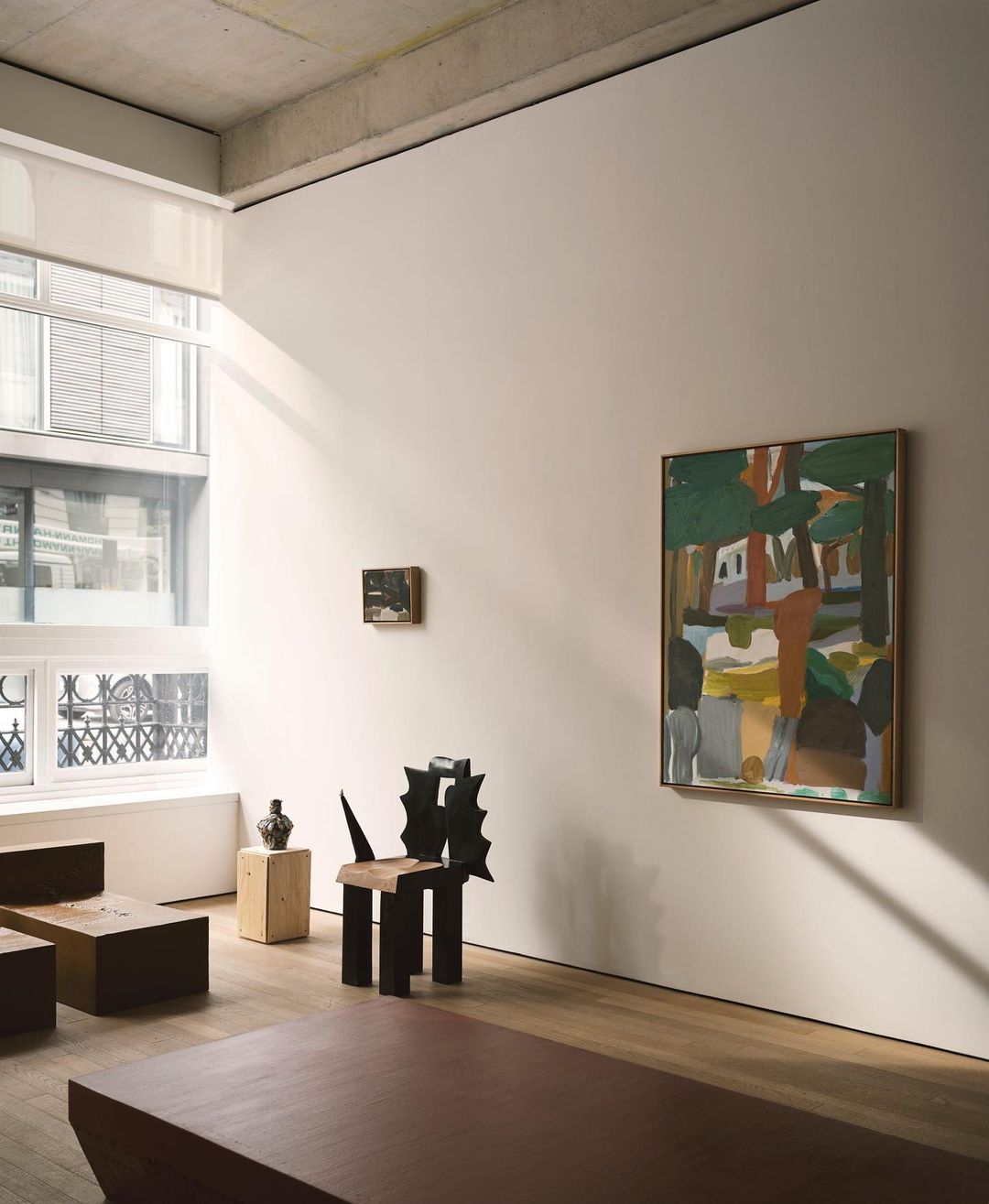 Modern art gallery with abstract paintings, contemporary chair, and wooden furniture in a bright, minimalist interior space with natural light.