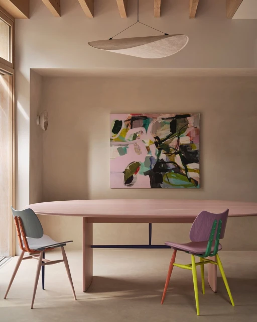 Dining room interior with abstract art, an oval table, and two chairs with multicolored legs under a modern disc-shaped pendant lamp.
