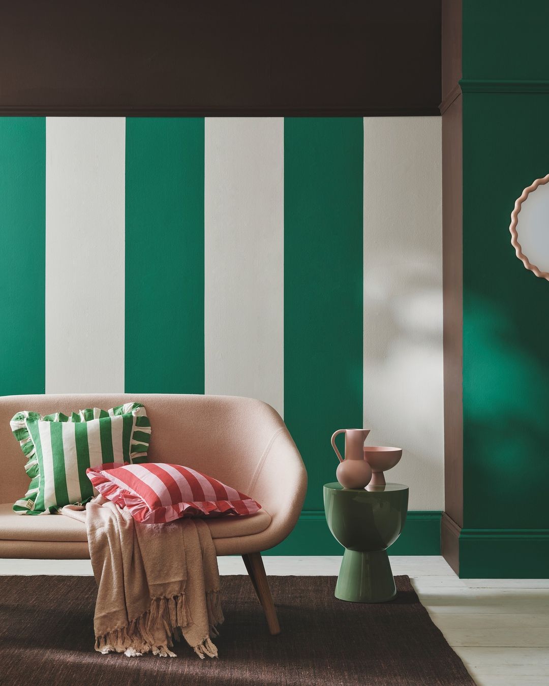 Interior design of a living room featuring a light pink sofa with striped pillows, a green side table with decor, and striped wallpaper.