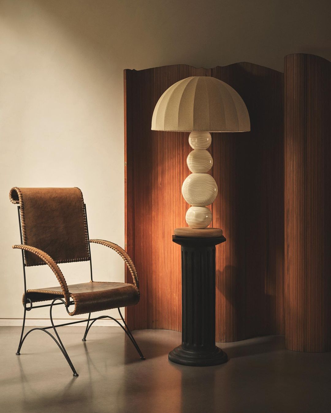 Stylish interior featuring a brown leather chair, a sculptural lamp on a black pedestal, and a wooden screen in warm, inviting light.