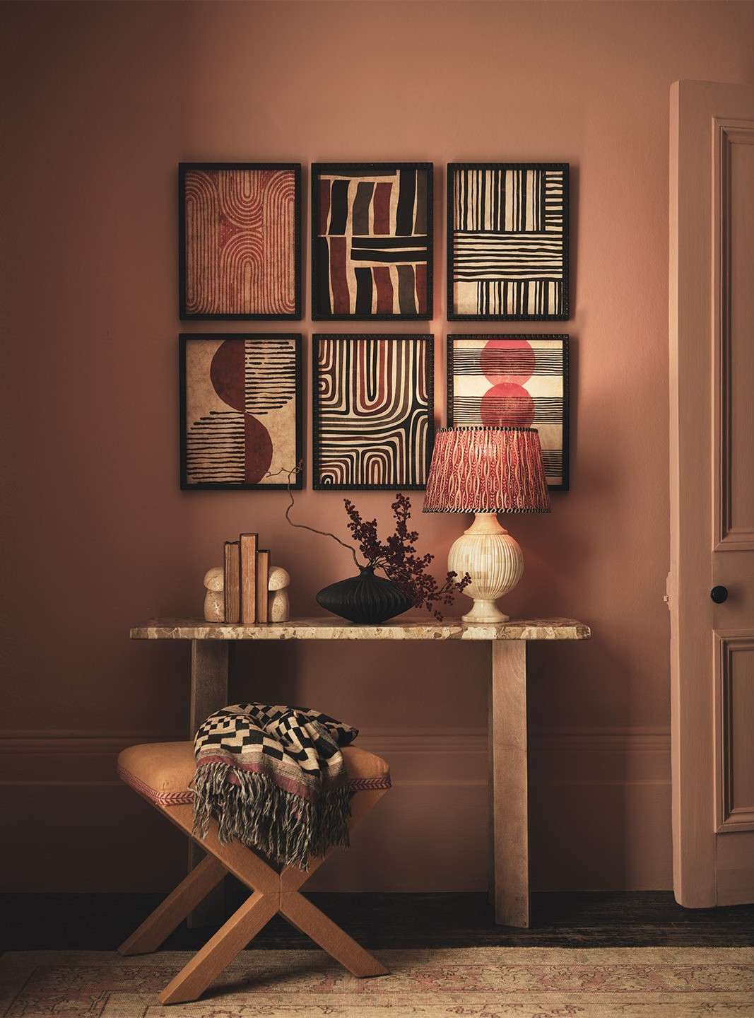 Interior design featuring six framed geometric art prints on a salmon wall above a marble-topped console table and upholstered stool.