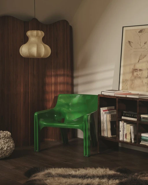 Interior of a room featuring a green plastic chair, a unique ceiling light, a wooden screen, and artwork displayed on the wall.