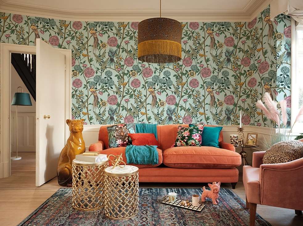 Living room interior with orange sofa, floral wallpaper, and various decorative objects creating a cozy, stylish atmosphere.
