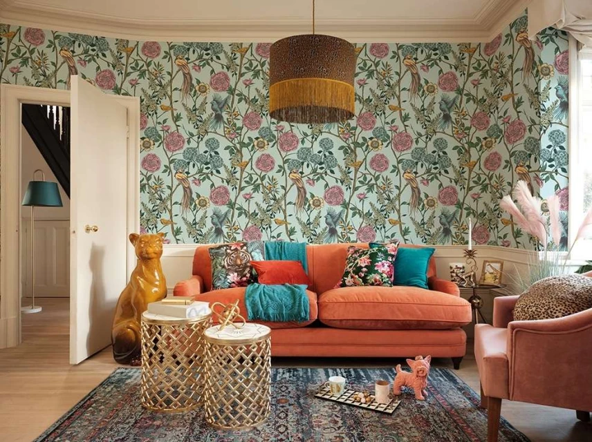 Living room interior with orange sofa, floral wallpaper, and various decorative objects creating a cozy, stylish atmosphere.