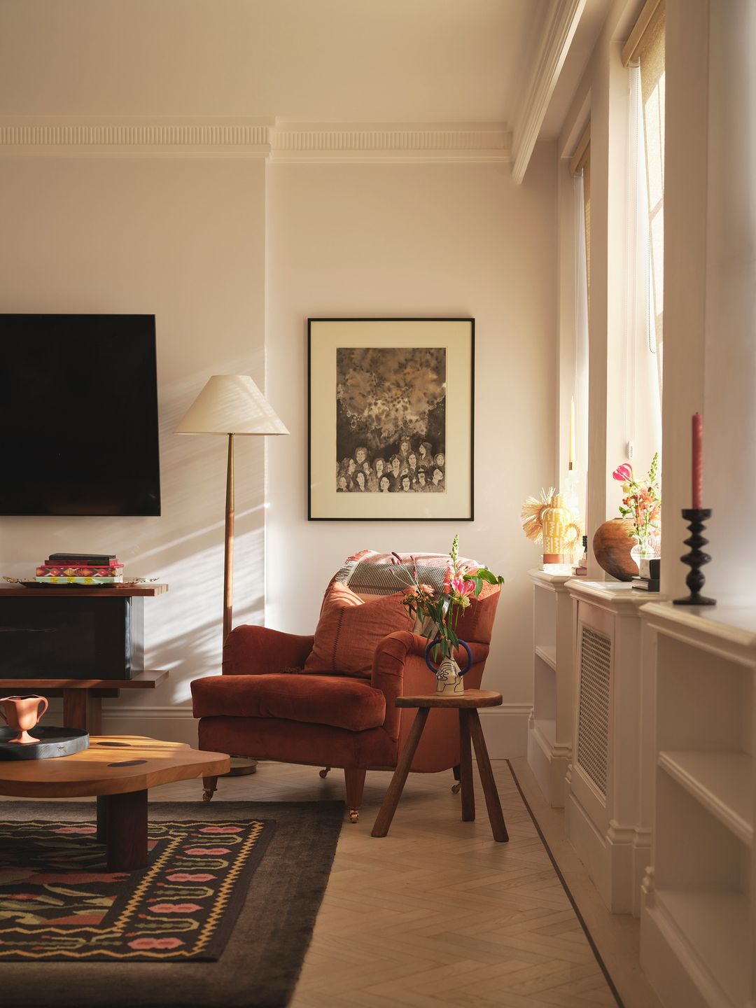 Warm sunlit living room featuring a rust orange velvet armchair, wooden coffee table, floor lamp, and framed artwork.