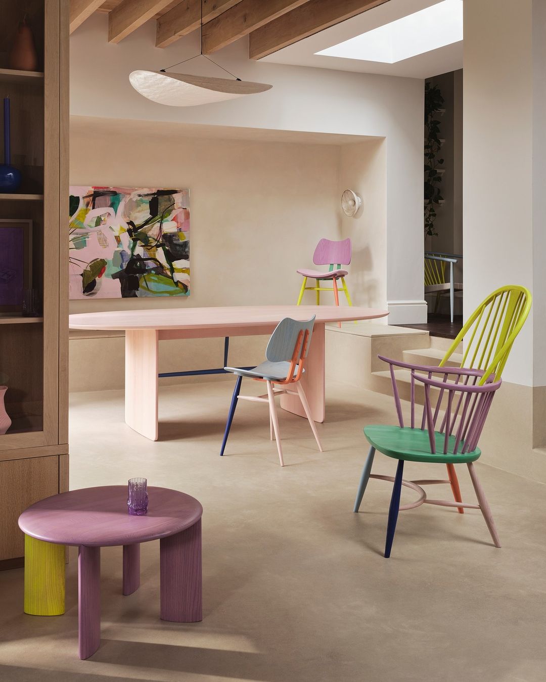 Eclectic pastel dining room with colorful chairs, pink table, and modern art. Natural light illuminates the minimalist interior design.