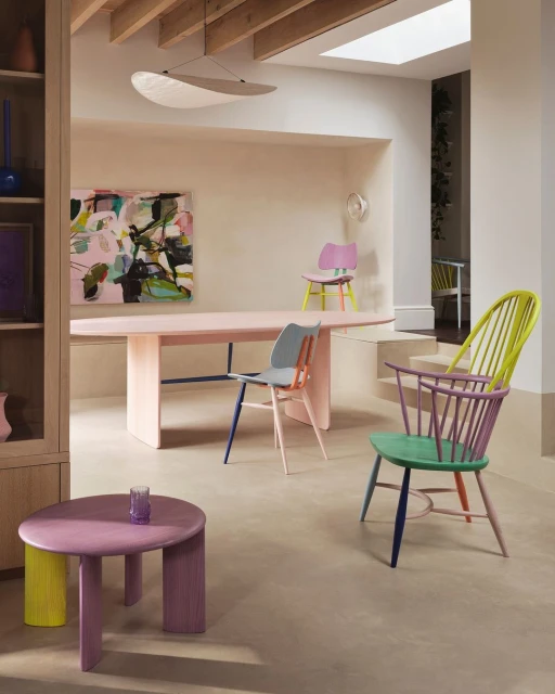 Eclectic pastel dining room with colorful chairs, pink table, and modern art. Natural light illuminates the minimalist interior design.