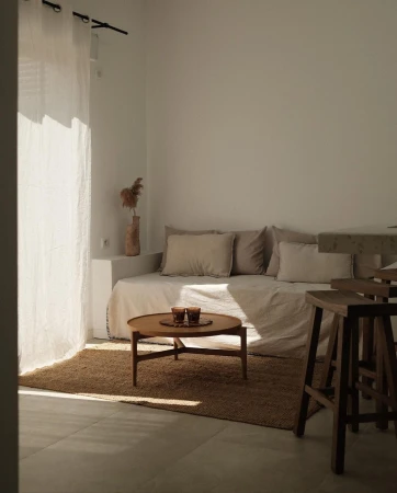 Minimalist living room interior with a daybed, round coffee table, seagrass rug, sheer curtains, and neutral color palette under natural light.