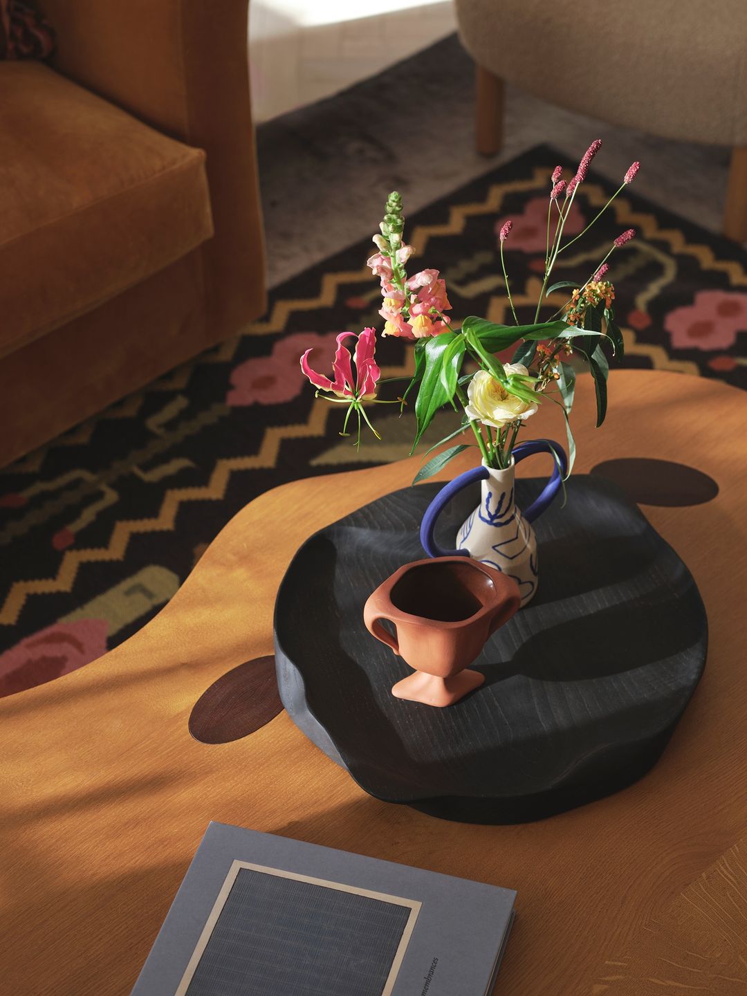 Still life of a table with flowers in a vase, a ceramic bowl, and a book in warm indoor lighting, casting shadows and enhancing textures.