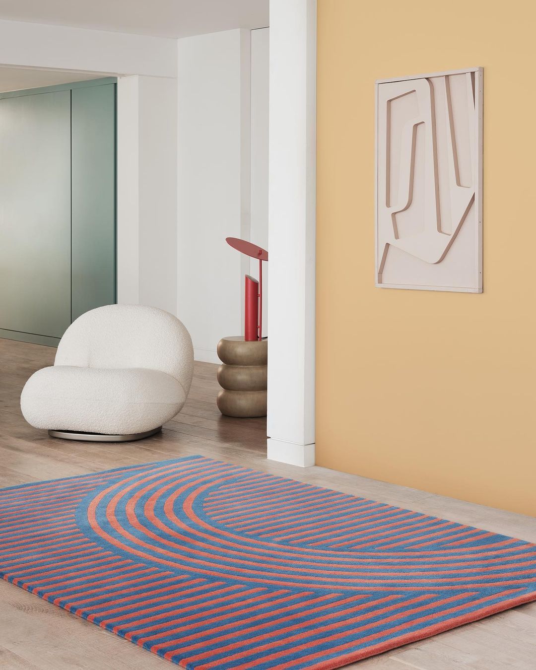 Interior view showcasing a blue and orange geometric patterned rug, off-white chair, and modern wall art in a minimalist setting.