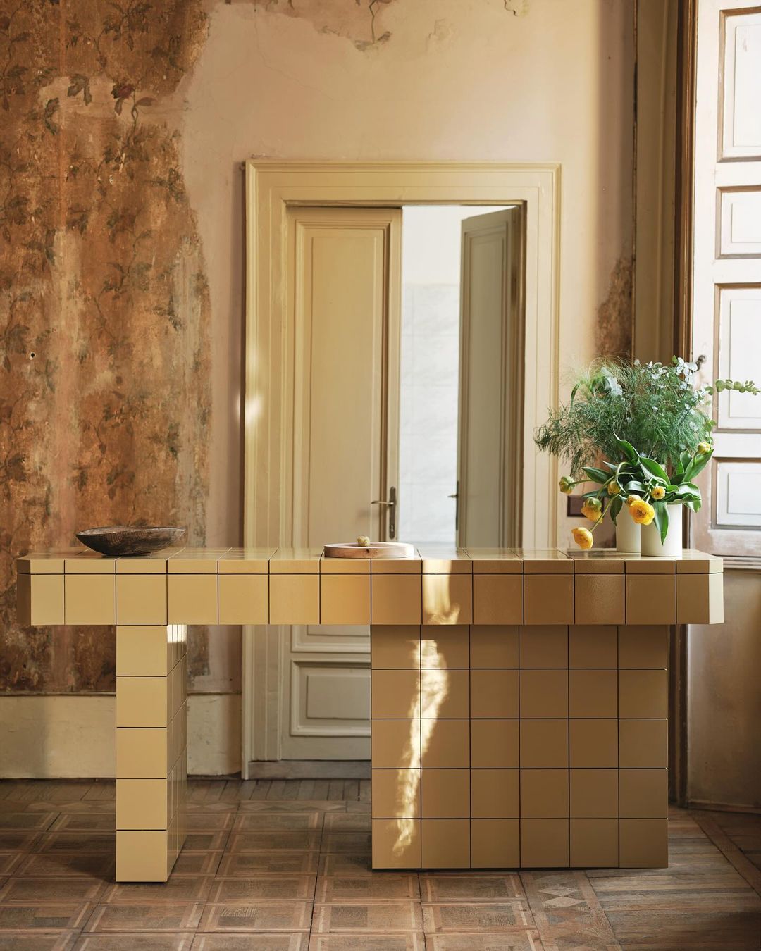 Tiled beige counter with a vase of green foliage and yellow flowers inside a rustic room by photographer Felix Speller
