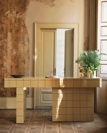 Tiled beige counter with a vase of green foliage and yellow flowers inside a rustic room by photographer Felix Speller