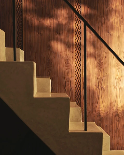 Close-up of modern staircase with beige steps and dark railing against a detailed wood-paneled wall, creating a warm interior scene.