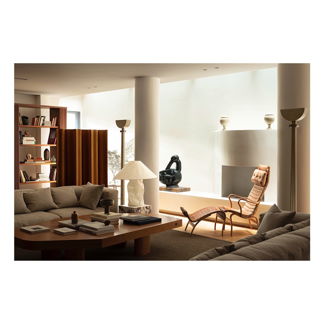 Living room interior featuring a grey sofa, coffee table, sculpture, chaise lounge, floor lamps, and a bookshelf creating a cozy space.