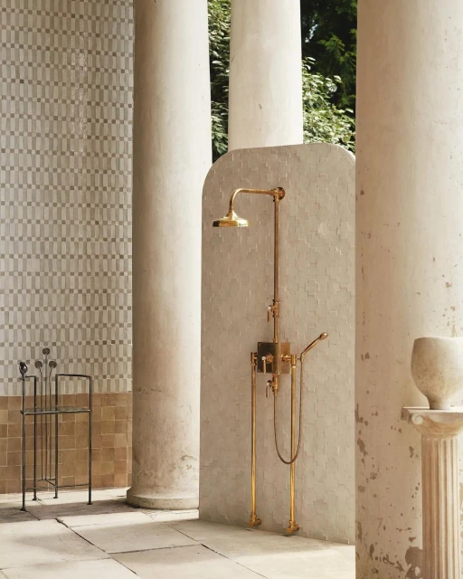 Indoor bathroom space featuring a gold shower fixture, columns, tile wall, and a towel rack.