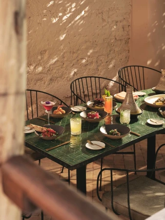 Outdoor dining table with multiple plates of food and drinks, covered with dappled sunlight, creating a cozy and inviting atmosphere.