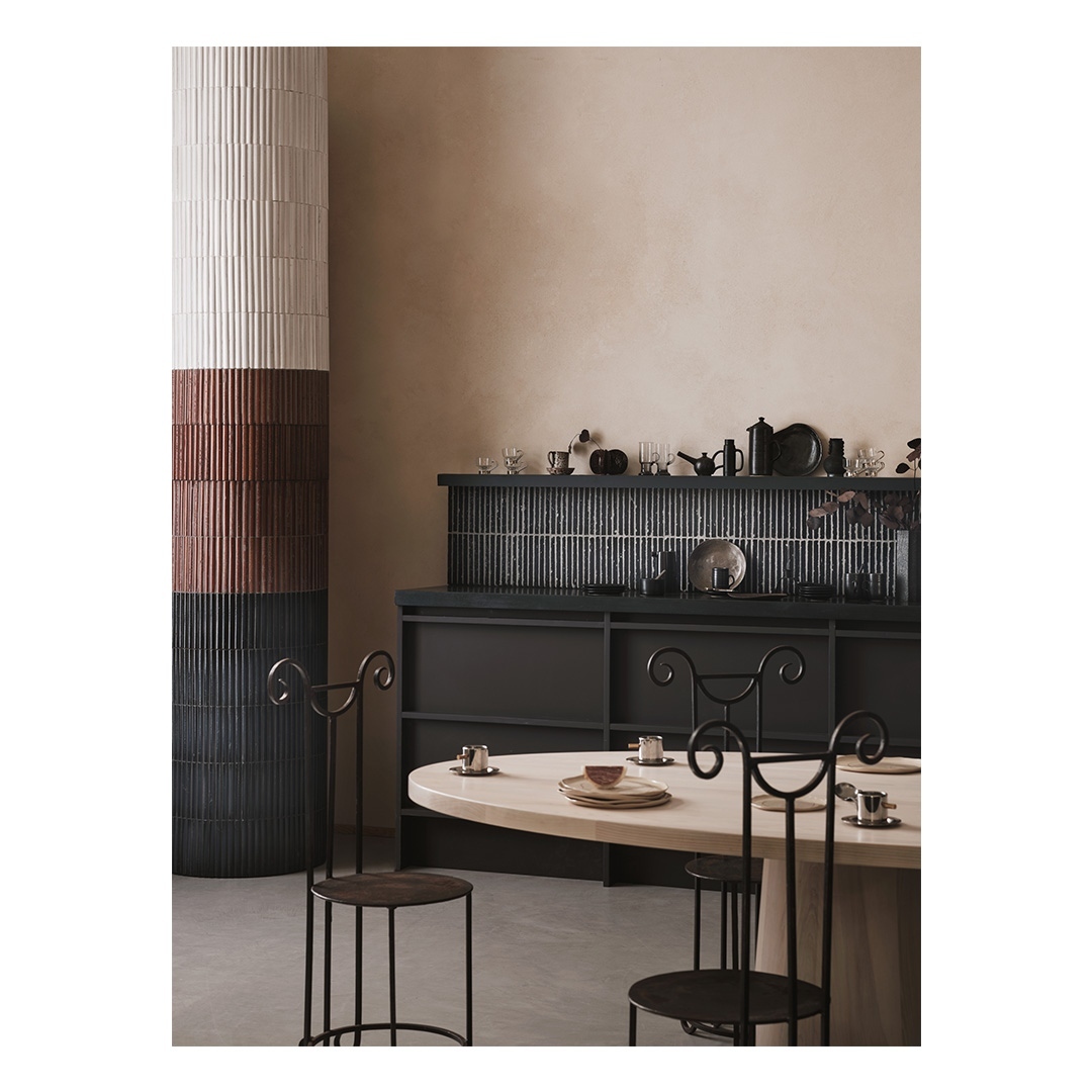 Interior view features a dining room with black chairs around an oval table, decorative shelving, and vertically ribbed panels.