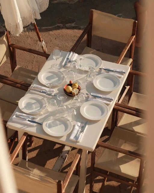 Overhead view of a white table set for six with plates, silverware, glasses, and a basket of lemons under a white umbrella.