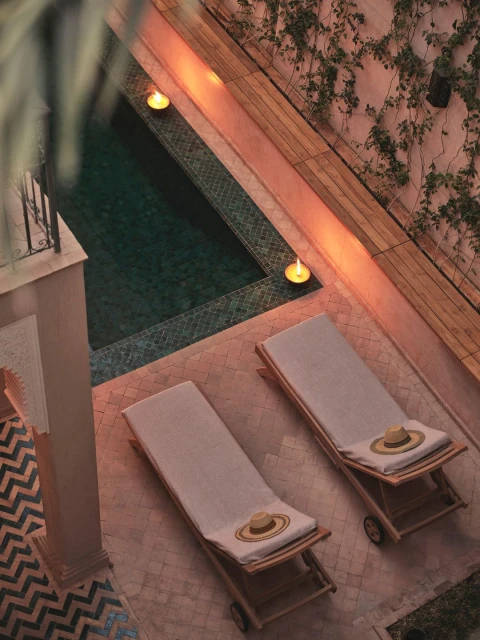 Overhead shot of a pool area with two lounge chairs with hats, ambient lighting, and lush vines on the walls creating a relaxing resort vibe.