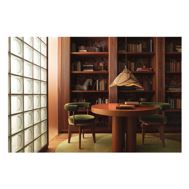 Interior design with round wooden table, green velvet chairs, pendant light, and bookshelf filled with books in a modern setting.