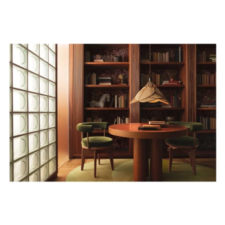 Interior design with round wooden table, green velvet chairs, pendant light, and bookshelf filled with books in a modern setting.