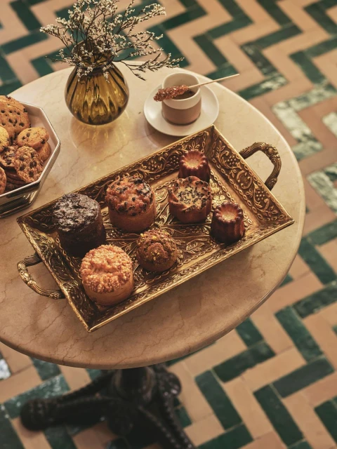 High-angle shot of an ornate gold tray with assorted pastries, a cup of coffee, and a vase with flowers on a marble table.